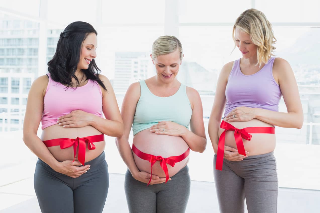 Cheerful pregnant women standing with red bow around bumps